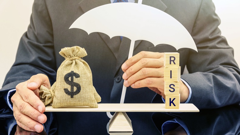 Financial risk assessment / portfolio risk management and protection concept : Businessman holds a white umbrella, protects a dollar bag on basic balance scale, defends money from being cheat or fraud