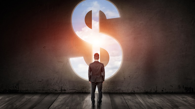 Well-dressed man standing in a big room in front of big silver dollar sign with blue sky inside it. Symbol of power, money and freedom. Targeting success and happiness. Back view.