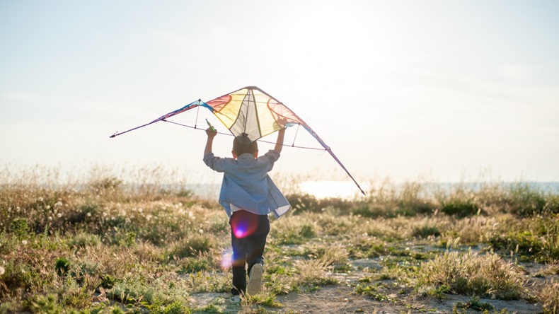 Brave new world concept of boy running with kite towards sunset sea horizon