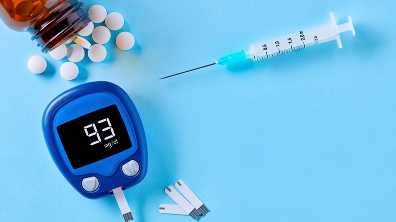 Diabetes monitoring and healthcare. Close up top down view of glucose meter, drug pills and syringe on blue background with copy space.