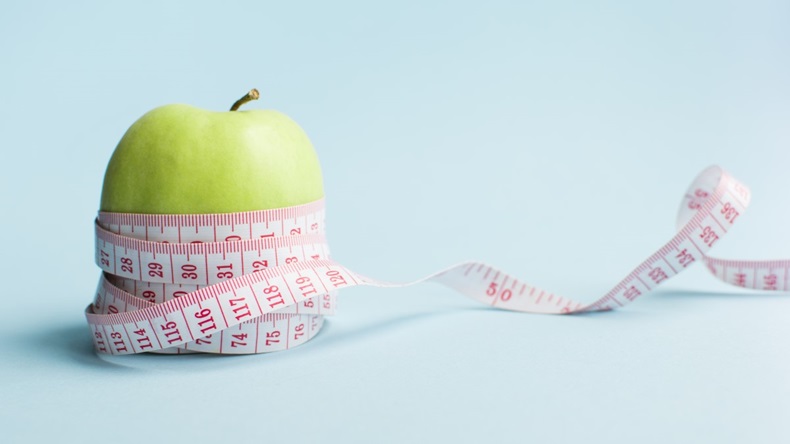 Apple with measuring tape on blue background. Weight loss, counting calories and healthy eating concept