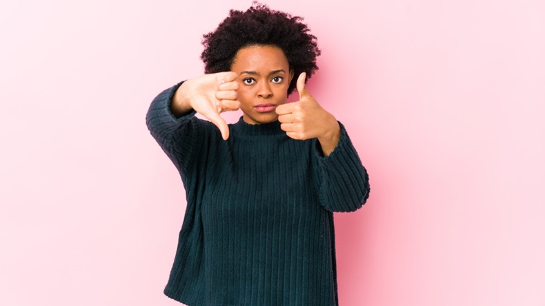 Woman with one thumb up and one thumb down against pink background, represents mixed views