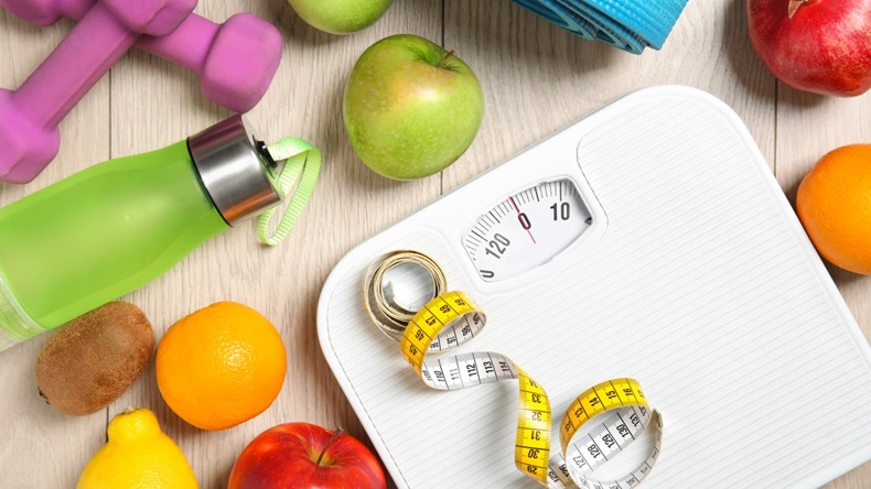 Weighing scales with measuring tape, fruits and dumbbells