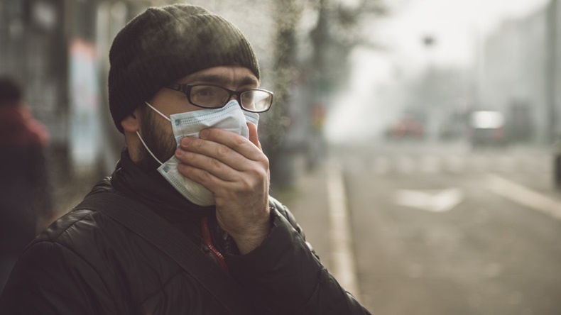 Man in polluted city holding a face mask over his face
