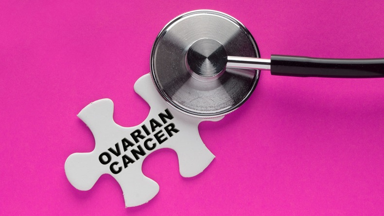Stethoscope on a white puzzle piece with a written word ovarian cancer on a pink background