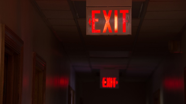 Two lighted glowing red exit signs in an office hallway with arrows pointing the way out of the building.