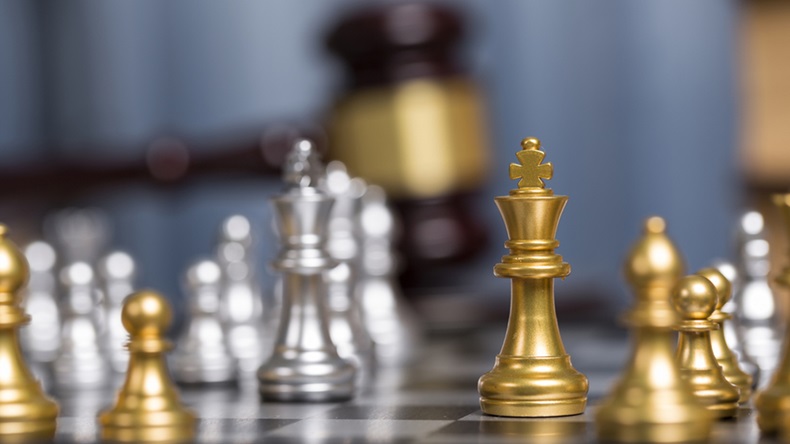Close up golden chess pieces with blurry judge gravel and law book background.
