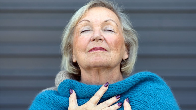 Attractive senior woman savoring the moment standing with her eyes closed and head tilted back with a serene expression as she clasps her chest with her hands